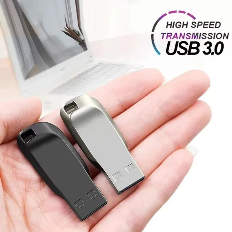 Hand holding two compact USB 3.0 flash drives in black and silver finishes against a blurred laptop background.