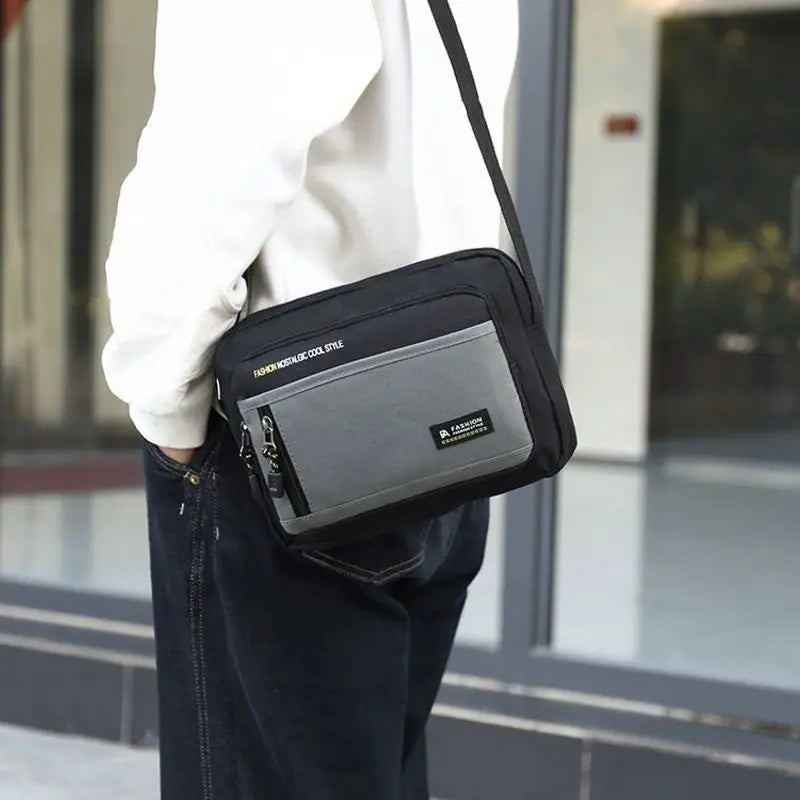 A man wearing a black and grey rectangular crossbody bag with an adjustable strap and front zip pocket.