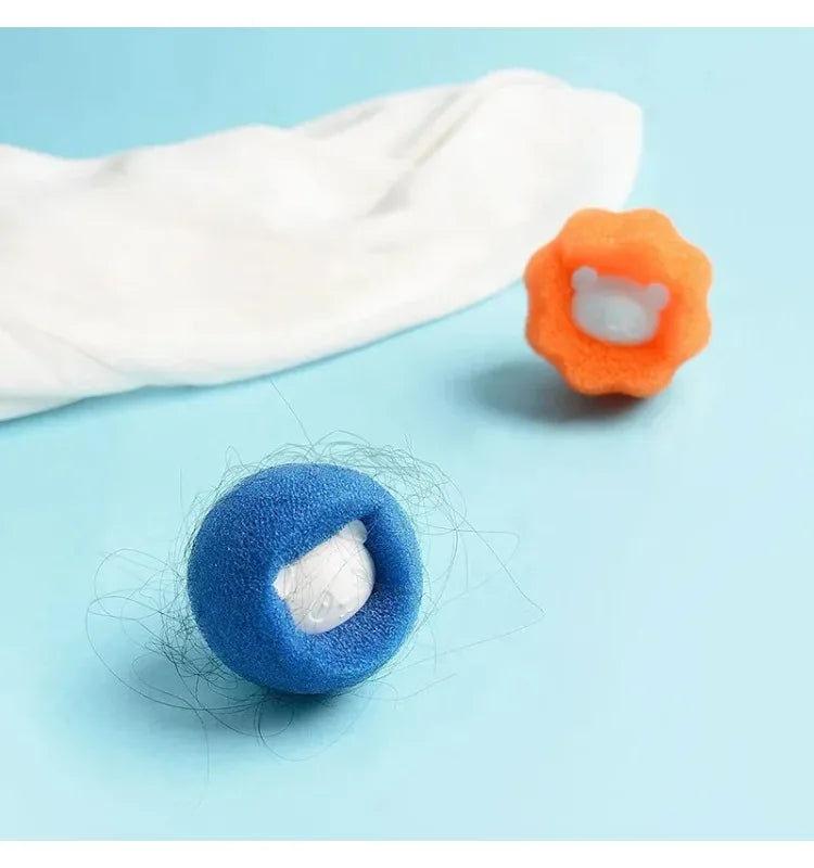 Blue and orange sponge laundry balls for hair and lint removal, with one ball catching stray fibres on blue surface.