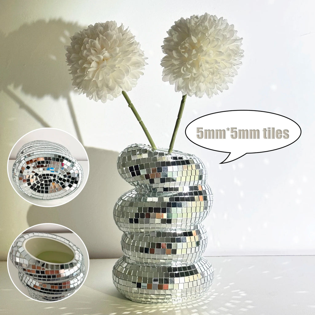 A tiered, reflective disco ball vase featuring small square mirror tiles, displayed with two white faux flowers.