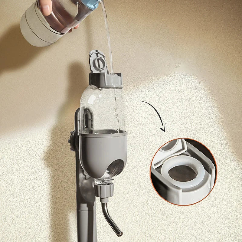 Gray hanging pet water bottle dispenser mounted on a wall, with water being poured into the top.