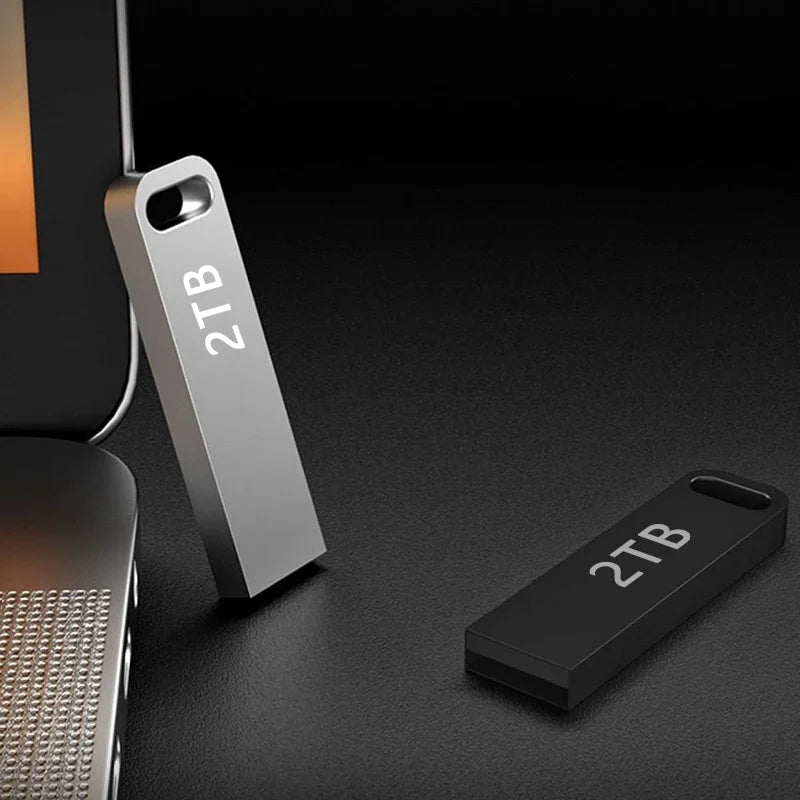 Sleek silver and black 2TB portable flash drives with a slim, key-ring design, shown next to a laptop.