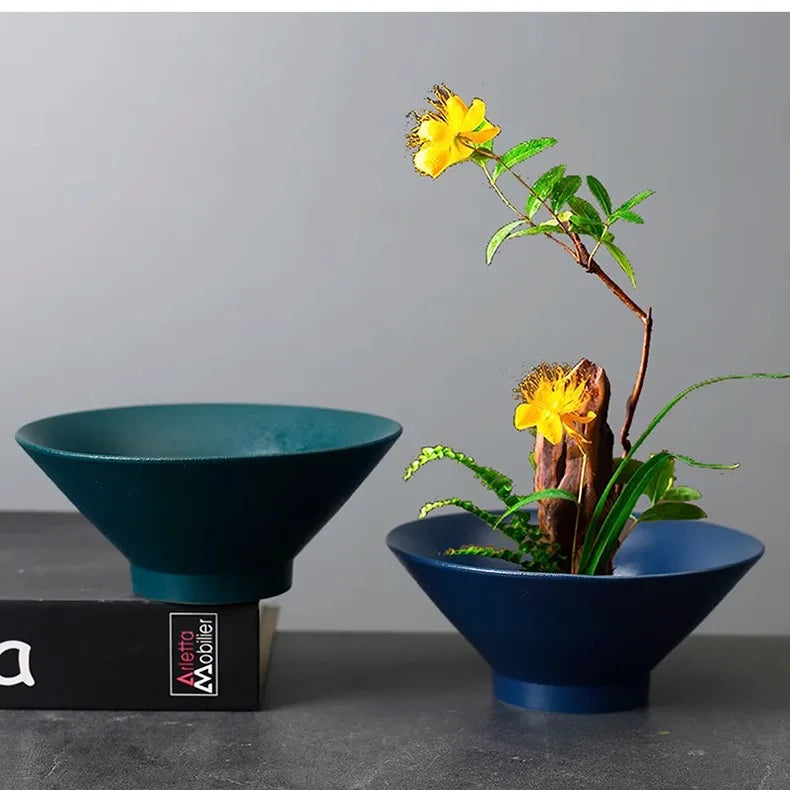Two minimalist teal and blue ceramic pedestal bowls for floral arrangements on a grey surface.