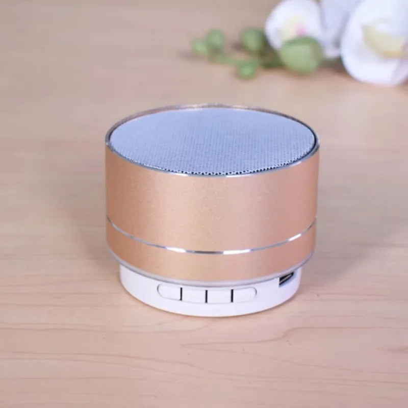 Compact rose-gold aluminium Bluetooth speaker with white control buttons and a metallic mesh top.