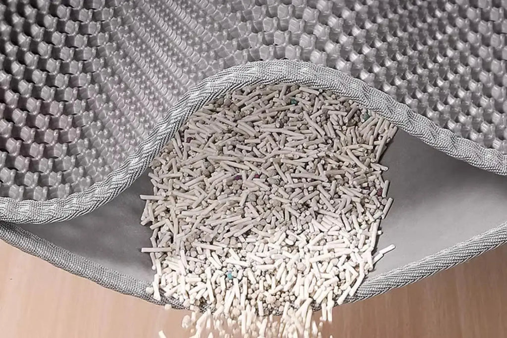 Grey dual-layer cat litter mat with honeycomb top and waterproof base, showing trapped litter being emptied.