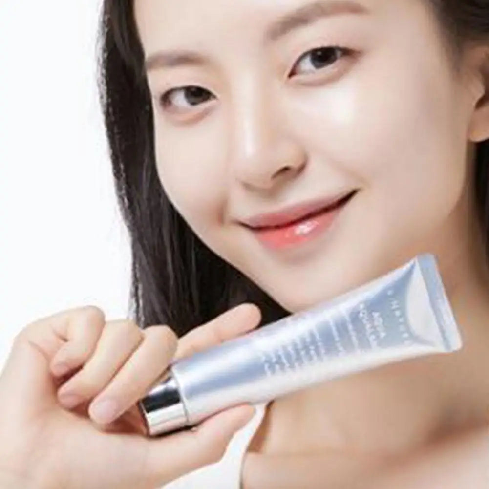A woman with glowing skin holding a silver, metallic skincare tube against a white background.