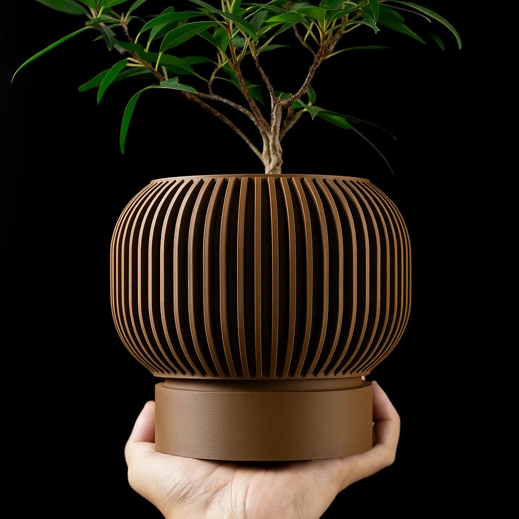 A hand holds a brown, 3D-printed, ribbed spherical plant pot containing a small green tree against a black background.