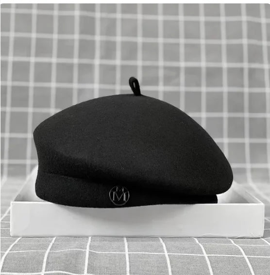 Classic black wool felt beret with a small stem top and a metallic letter 'M' logo detail on the front.