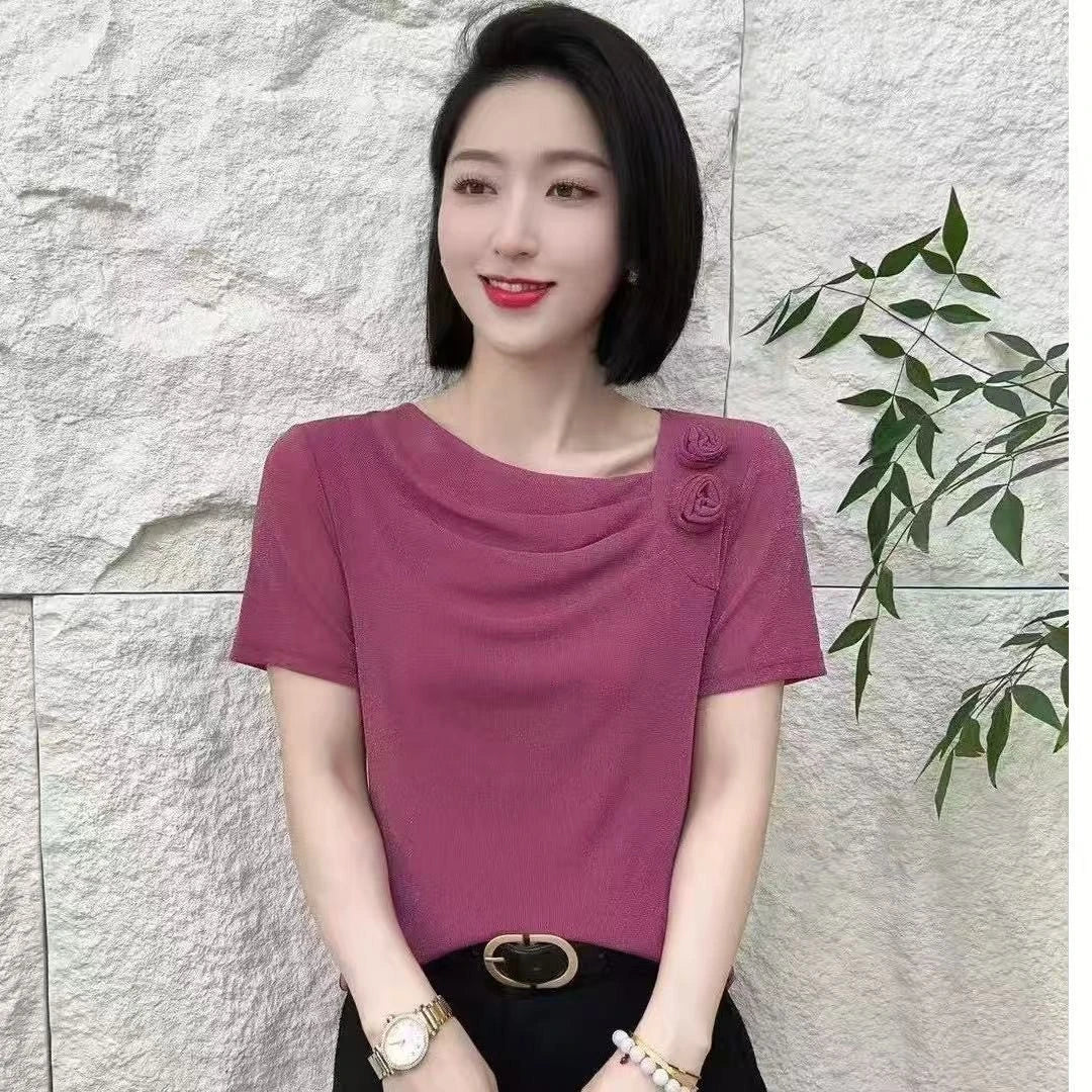 Woman wearing a short-sleeved mauve blouse with draped neckline detail and fabric rose embellishments.