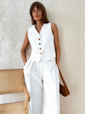 Model wearing a chic white linen-blend vest with brown buttons, paired with matching high-waisted wide-leg trousers.