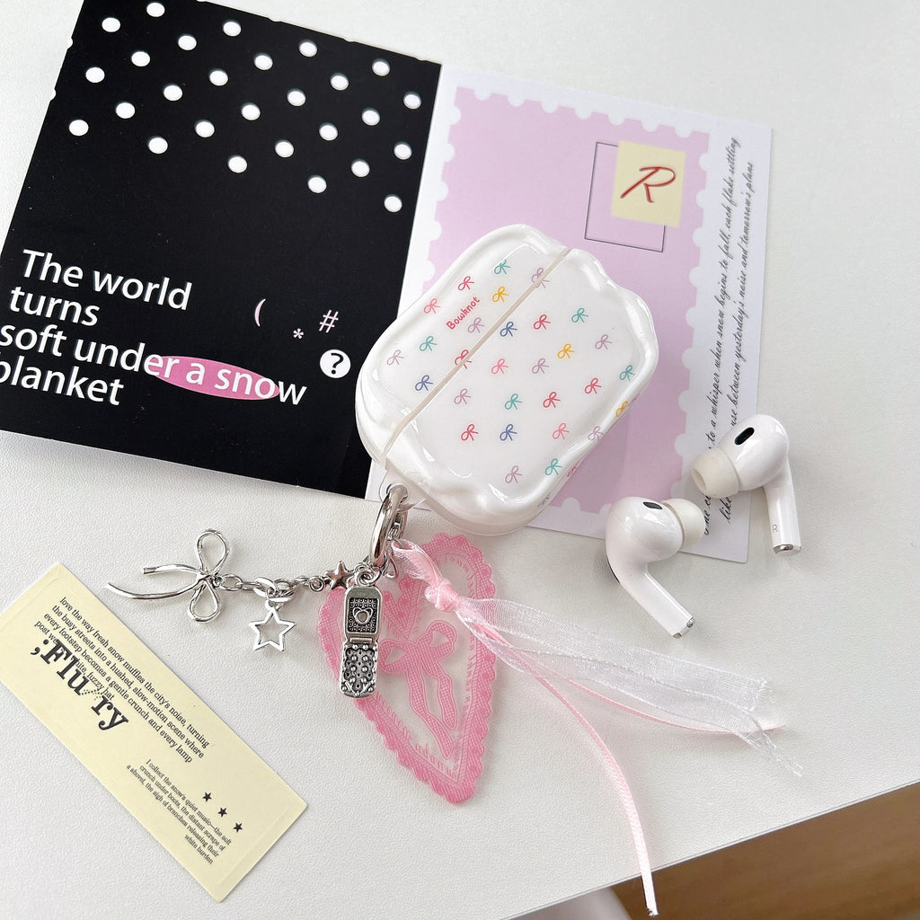 White AirPods Pro case featuring a colourful bow print, scalloped edges, and a decorative heart and charm keyring.