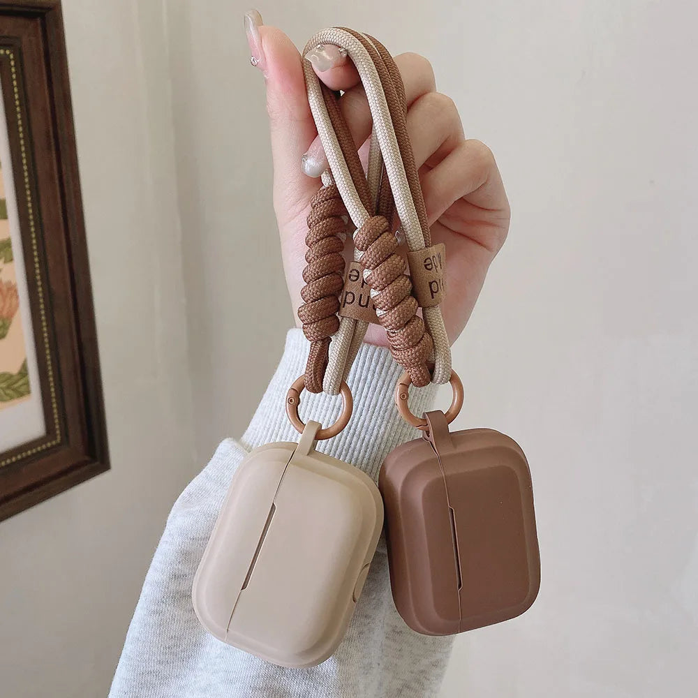 Two beige and brown silicone AirPods cases with braided wrist straps held in a hand.