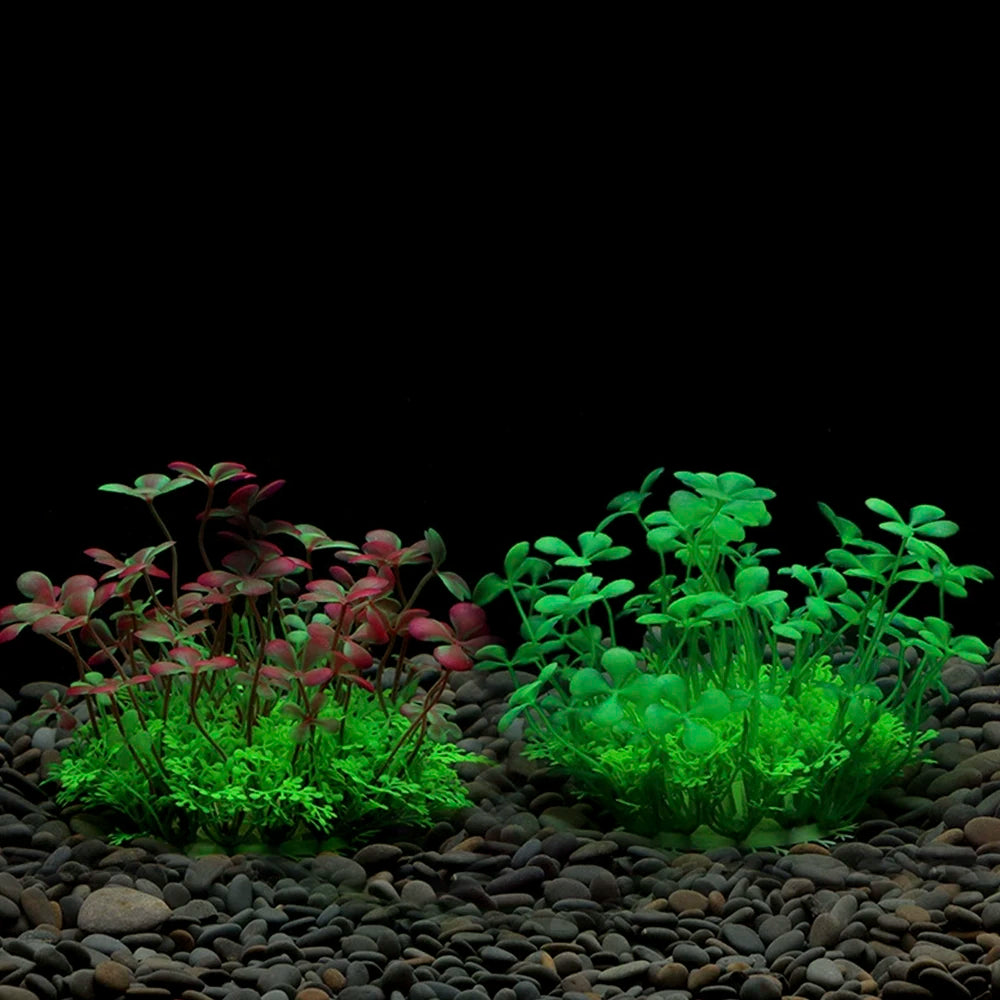 Two artificial aquarium plants with clover-like leaves, one red-tipped and one bright green, on a bed of dark gravel.