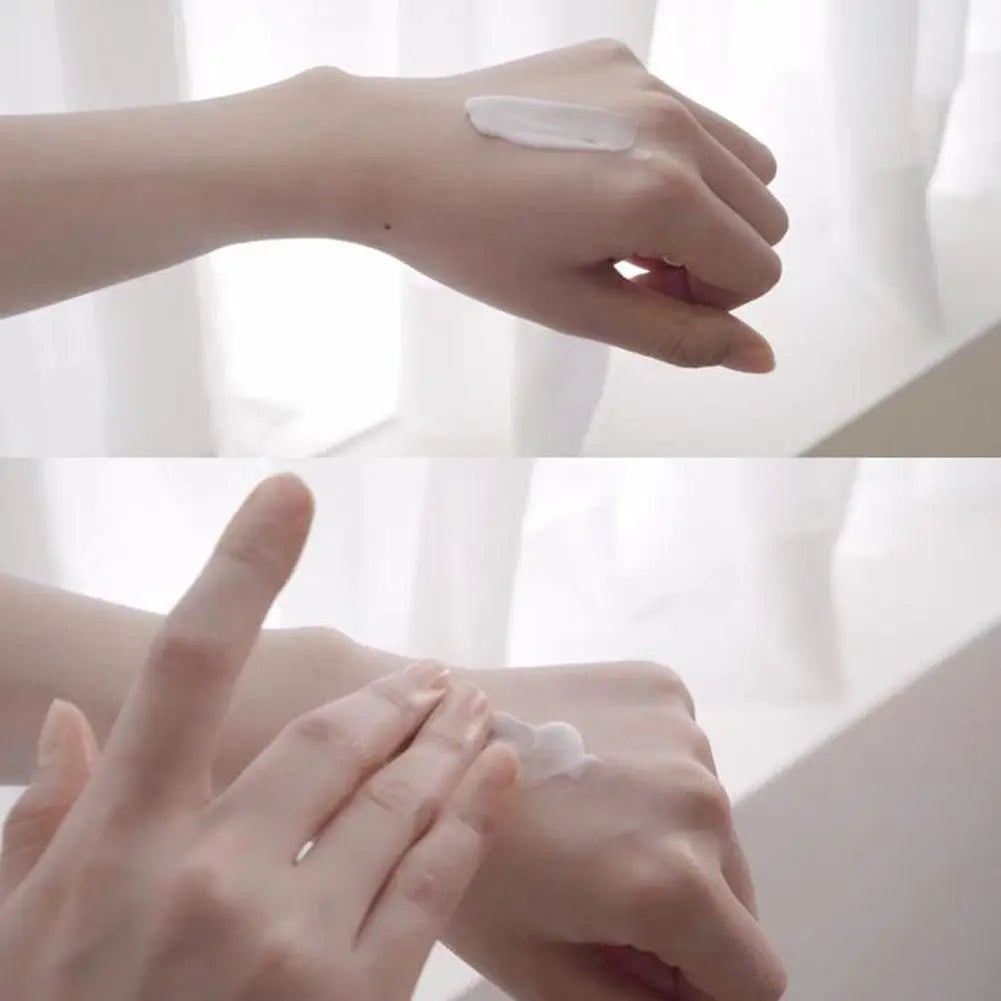 A smooth, white skincare cream being applied to the back of a hand in a bright, minimalist setting.