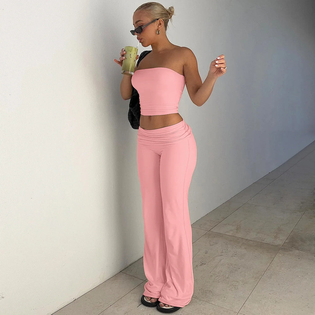 Woman wearing a baby pink bandeau crop top and matching low-rise flared trousers, standing in a hallway.