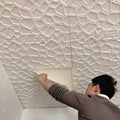 A person installing off-white, 3D self-adhesive wall tiles featuring a modern, abstract geometric lattice pattern.