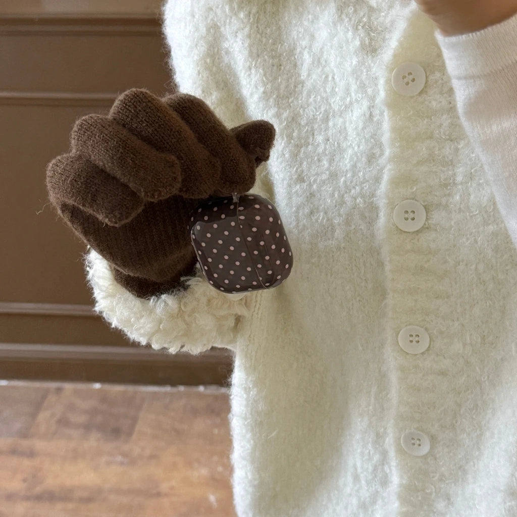 Brown polka dot hard shell case for AirPods, held in a hand wearing a brown knitted glove.