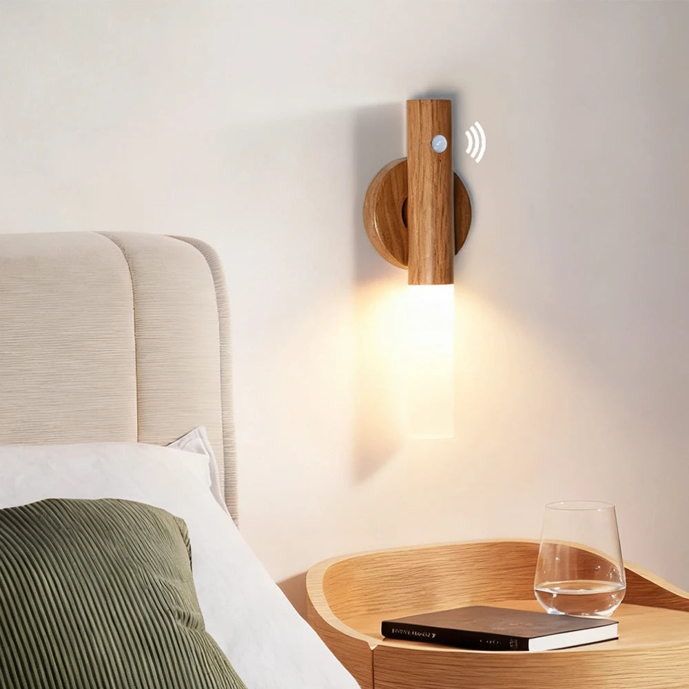 Minimalist wooden magnetic wall light with motion sensor and warm LED glow mounted above a bedside table.