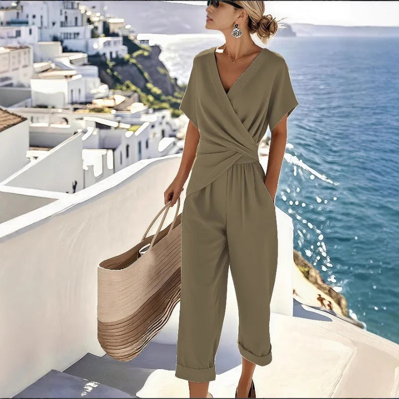 Woman wearing a khaki, V-neck wrap-front jumpsuit with short sleeves, cropped cuffed legs, and side pockets.