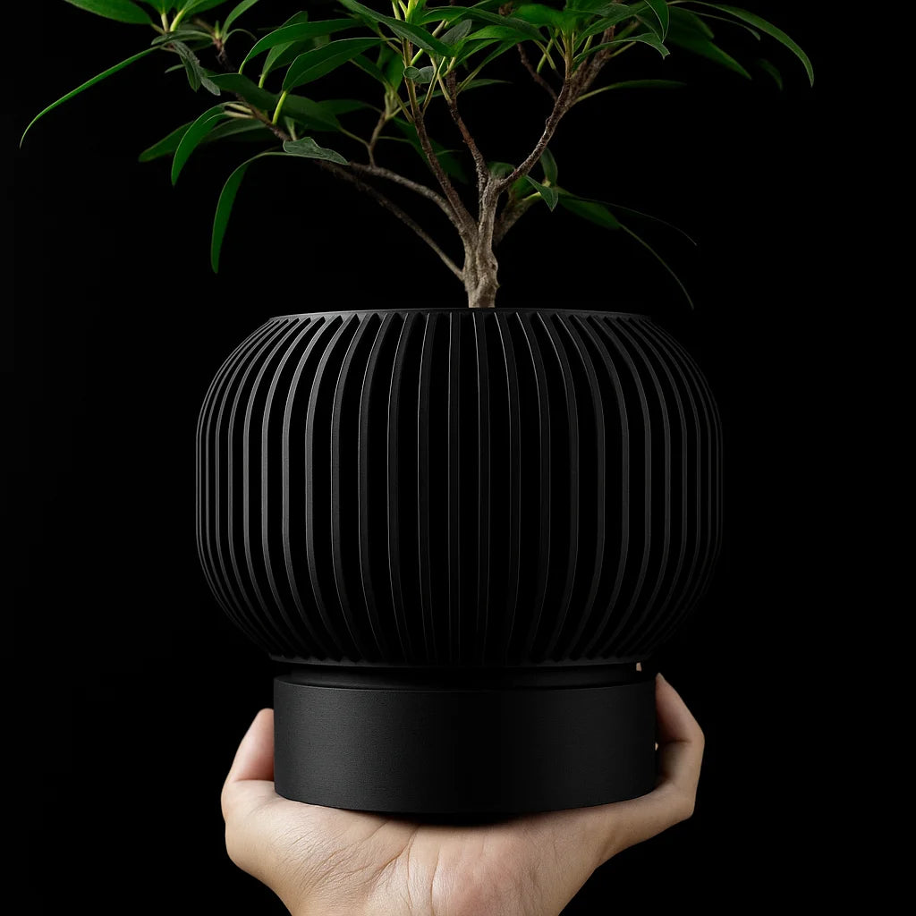A hand holds a matte black, 3D-printed plant pot with vertical ribbed texture and a smooth base, containing a plant.