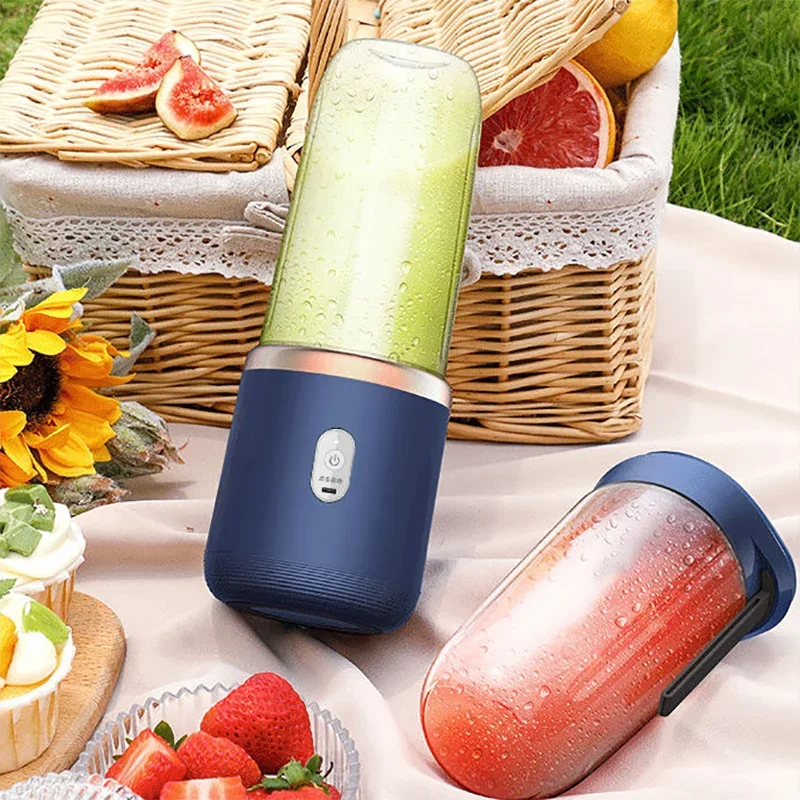 Portable navy blue personal blender with clear container on a picnic setup with fruit and flowers.
