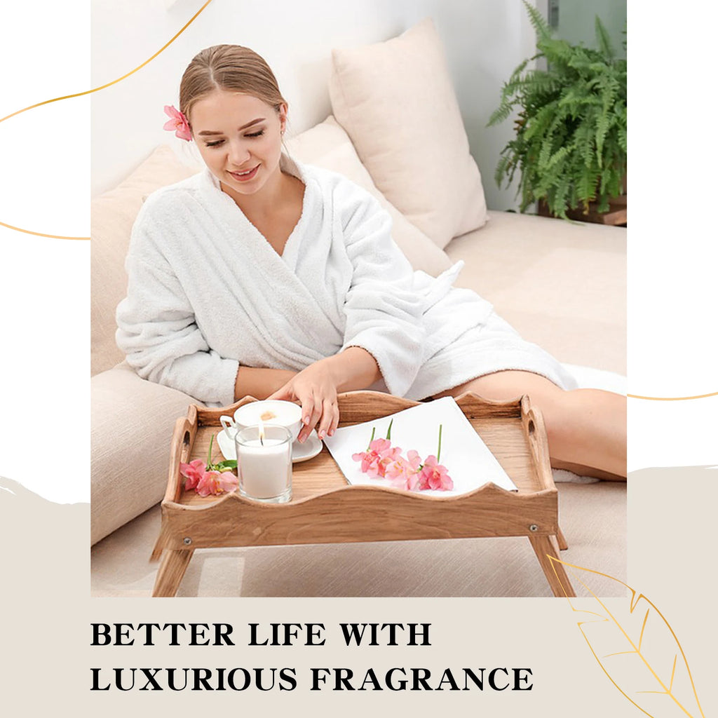 Woman in white robe on a bed with a wooden tray holding a lit candle, teacup, and pink flowers.