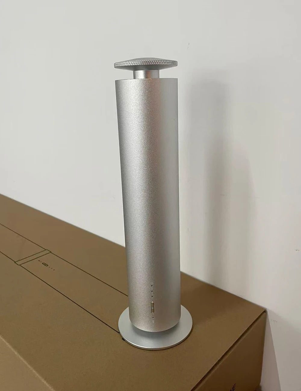 Minimalist silver cylindrical aroma diffuser with a textured top dial, standing on a circular base.
