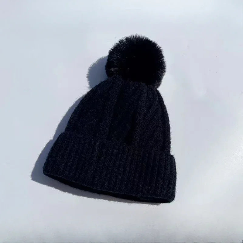 Black cable-knit beanie hat with a matching faux-fur pom-pom and a ribbed turn-up hem.