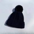 Black cable-knit beanie hat with a matching faux-fur pom-pom and a ribbed turn-up hem.