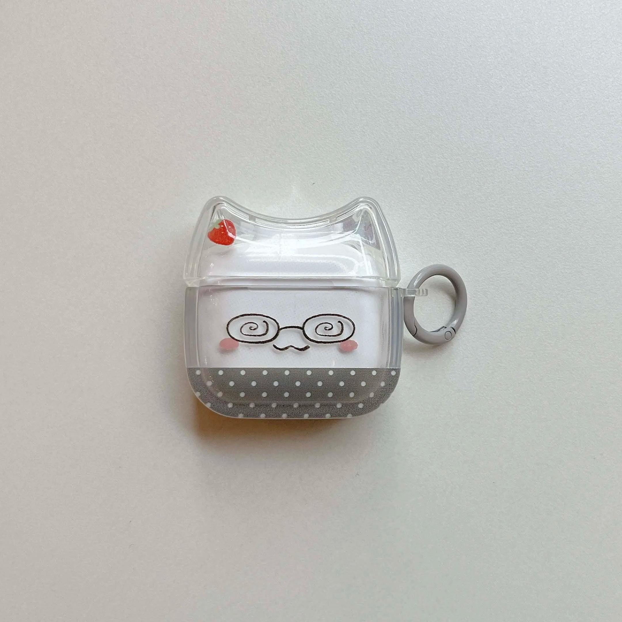 Clear cat-ear AirPods case with strawberry, glasses, and polka dot design. Includes grey carabiner.