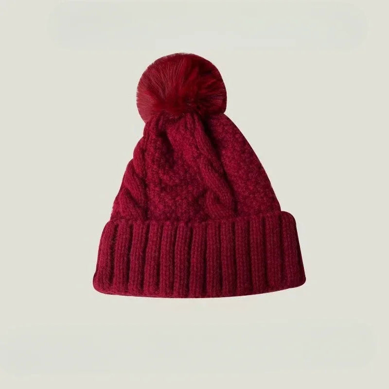 Deep red knitted winter beanie featuring a matching faux-fur pom-pom, cable knit pattern and a ribbed turn-up hem.