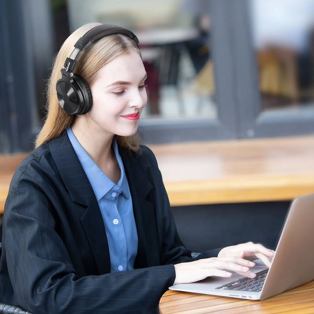 A professional woman wears sleek, black over-ear wireless headphones while working on a laptop.