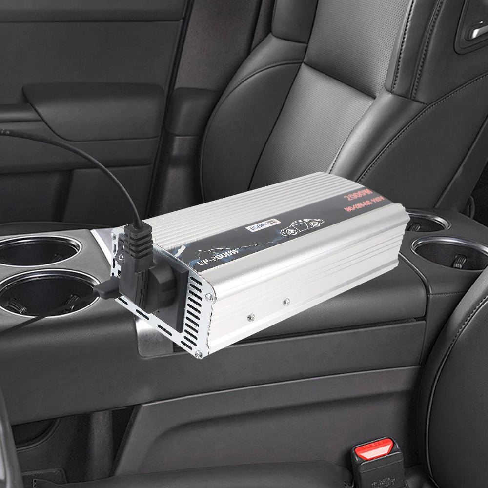 Silver 2000W car power inverter with USB port and plug socket, positioned on a centre console in a vehicle.