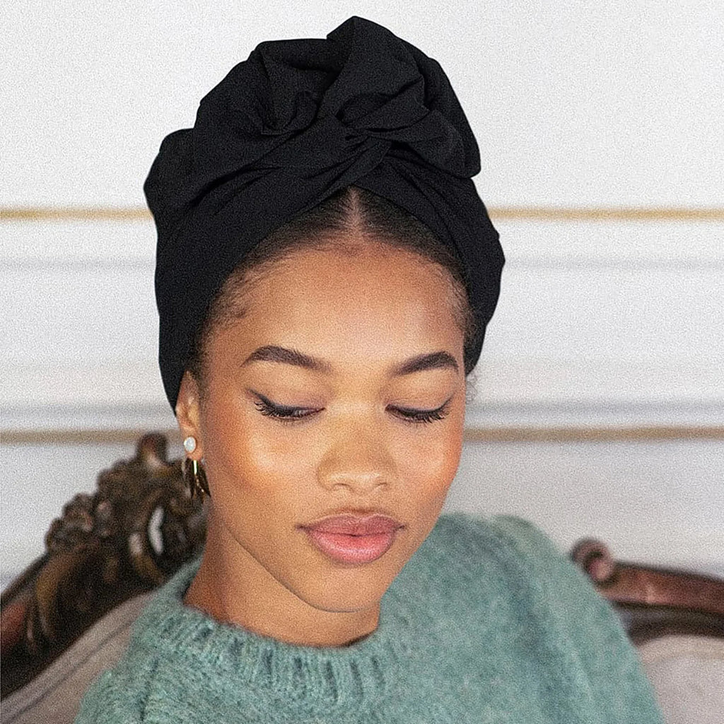 Elegant black vintage-style turban hat featuring a decorative knotted front design on a model.
