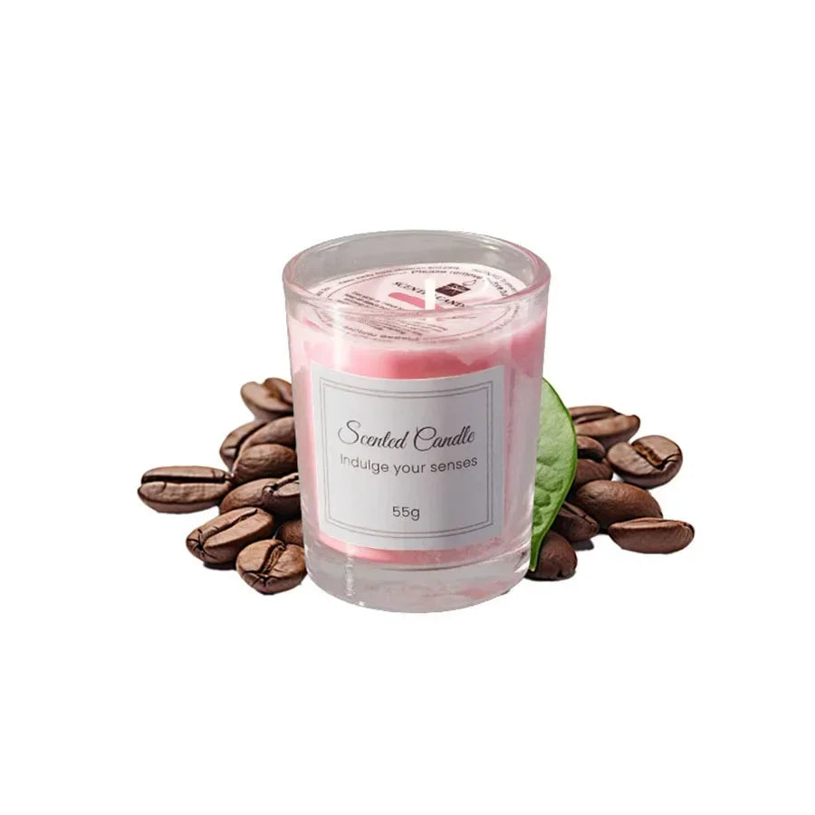 Pink scented candle in a glass votive, surrounded by coffee beans and a green leaf.
