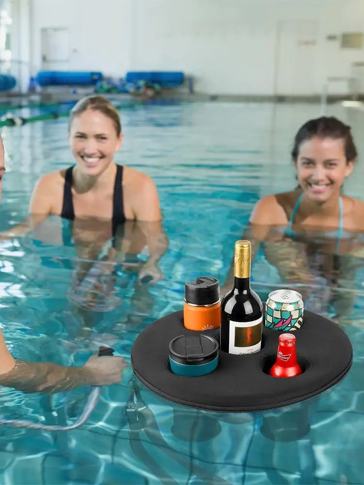 A black round floating cup holder in a pool, holding a wine bottle, can, cups, and a beer bottle.