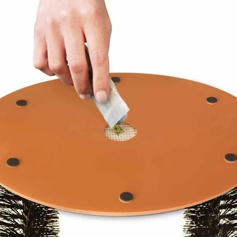 Hand pouring catnip into the centre of a round orange grooming arch base with black non-slip feet.