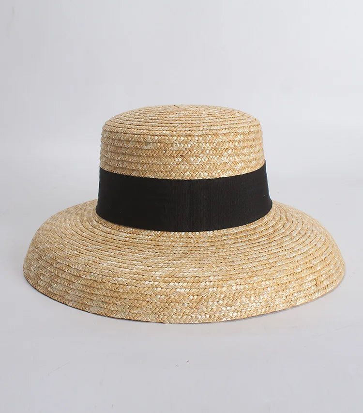 Elegant wide-brim straw sun hat in natural tan featuring a classic flat top and a wide black ribbon band.
