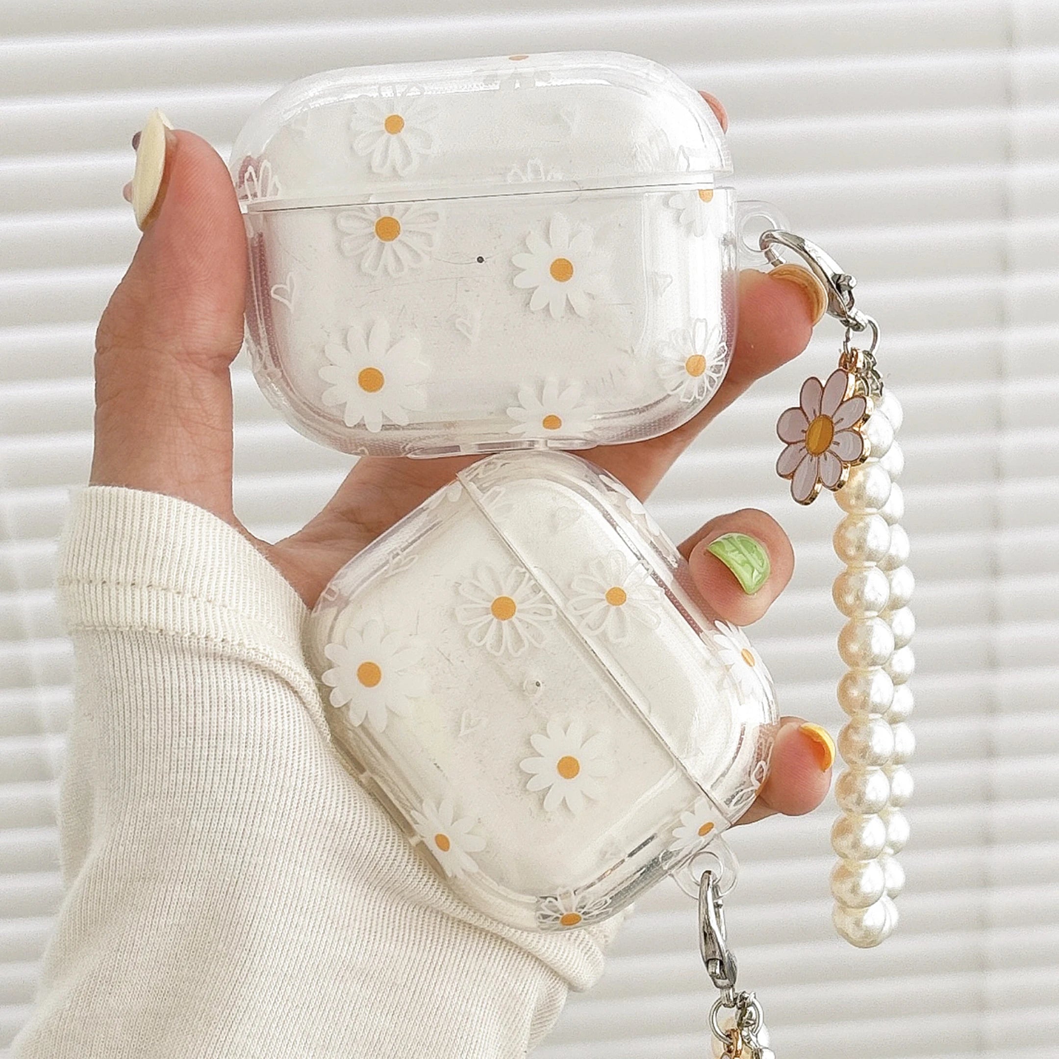 Clear plastic AirPods Pro case featuring a white daisy print and a pearl beaded charm strap.