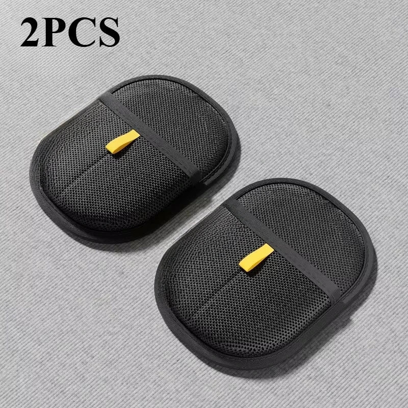 Two black oval mesh sponges with central elastic straps and yellow pull tabs on a grey background.