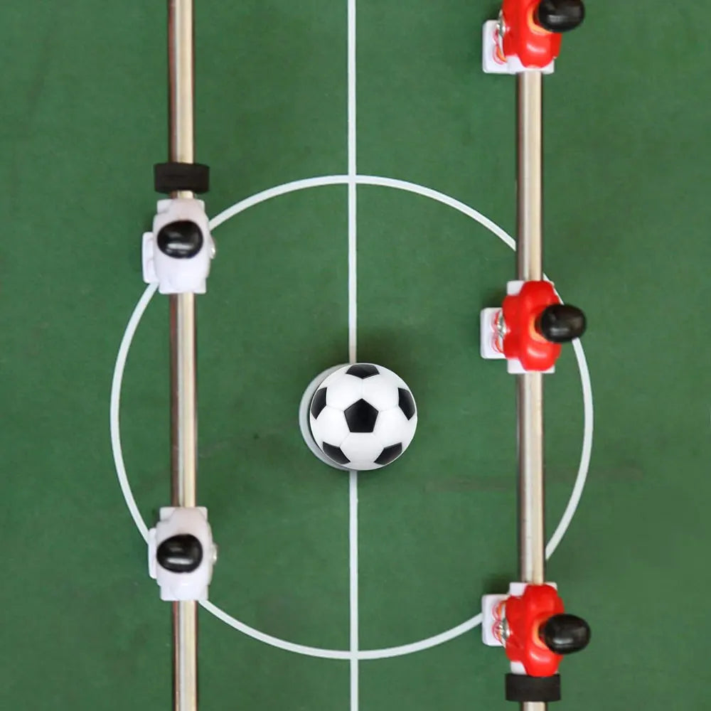 Top-down view of a foosball table featuring red and white player figures with a black and white ball in the centre.