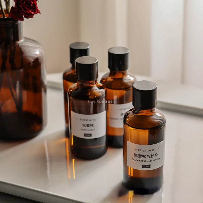 Four amber glass 50ml essential oil bottles with black caps and minimalist white labels on a white tray.