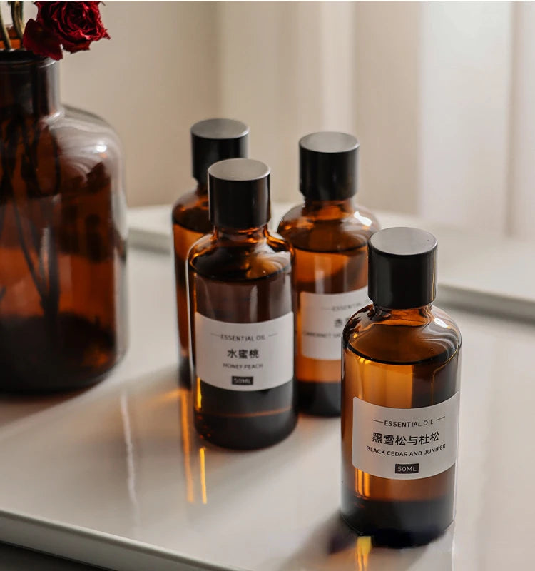 Amber glass 50ml essential oil bottles with black caps and minimalist white labels, arranged on a white tray.