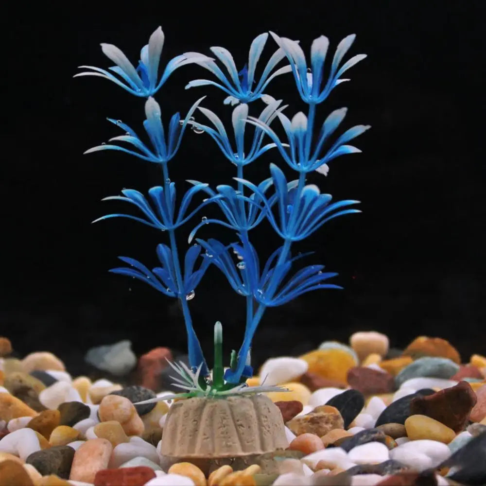 Artificial blue plastic aquarium plant with white-tipped leaves, anchored in a beige base on multi-colored gravel.