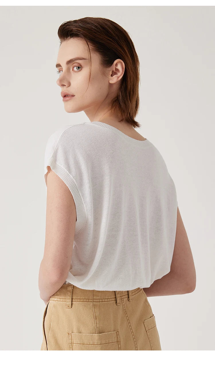 Woman wearing a crisp white, round-neck sleeveless knit top with ribbed armholes and tan trousers.