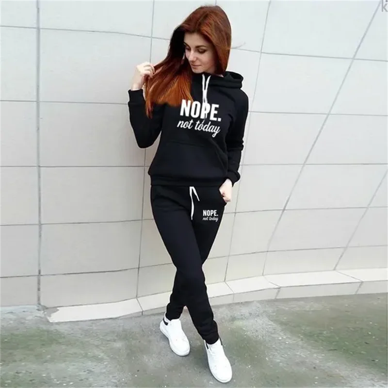 Woman wearing a black loungewear set featuring a hooded sweatshirt and joggers with "NOPE. not today" printed in white.