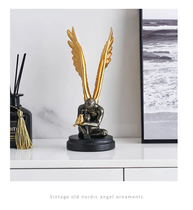 Vintage-style resin statue of a kneeling angel with large gold wings, holding a gold bird, on a black base.