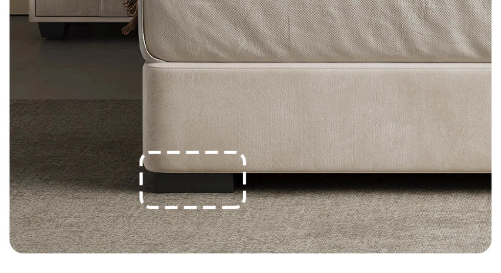 Close-up of a modern beige upholstered storage bed with a low-profile dark block foot on a carpeted floor.