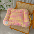 Pink and yellow gingham pet mat with raised bolsters, placed on a wooden woven chair.