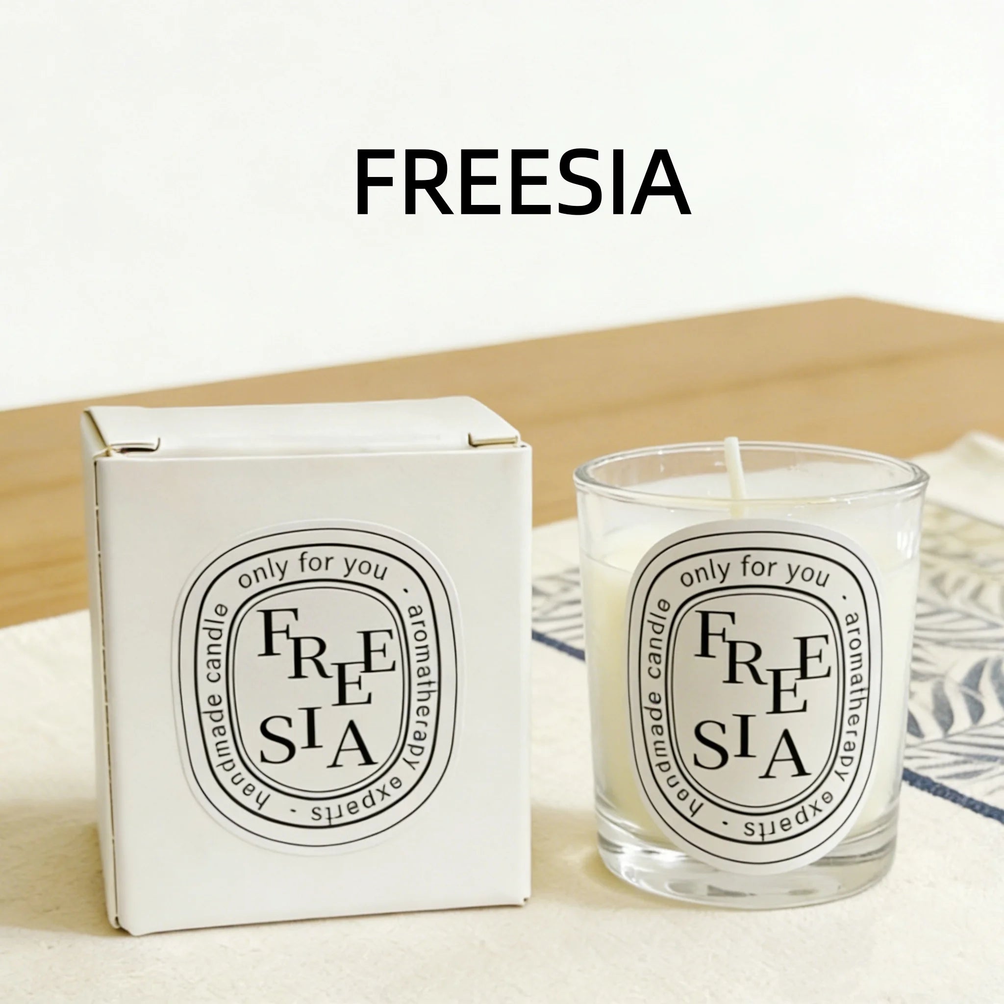 Freesia-scented handmade aromatherapy candle in a glass votive with matching white gift box and decorative label.